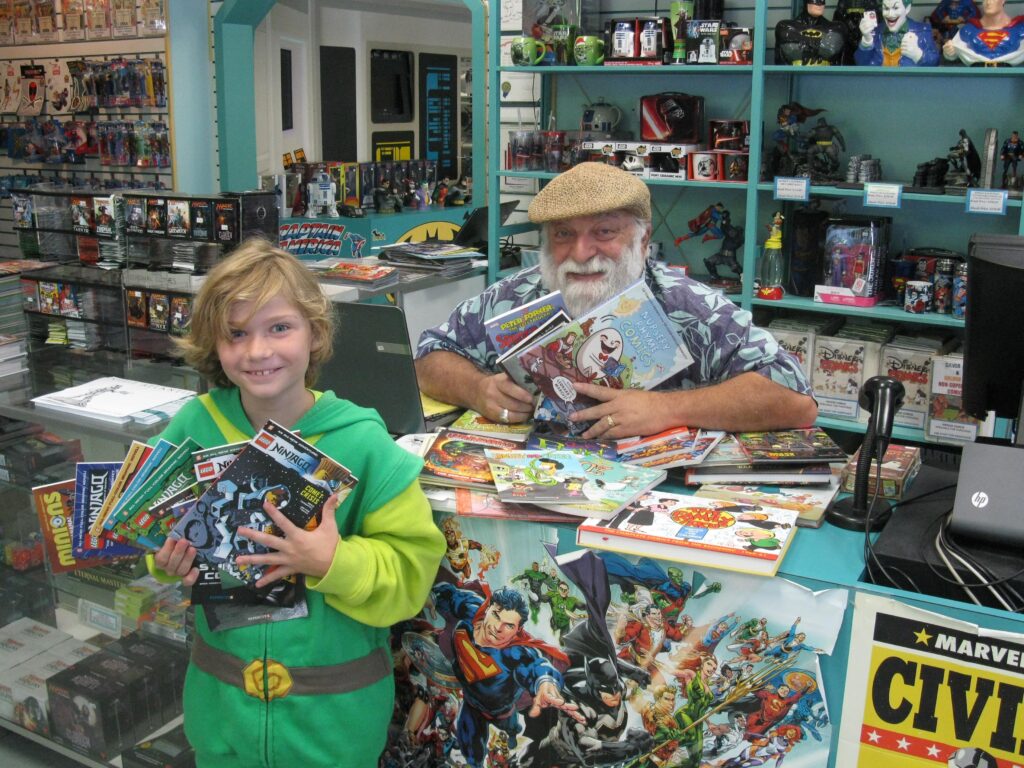 Joe holding up books with a young Atlantean